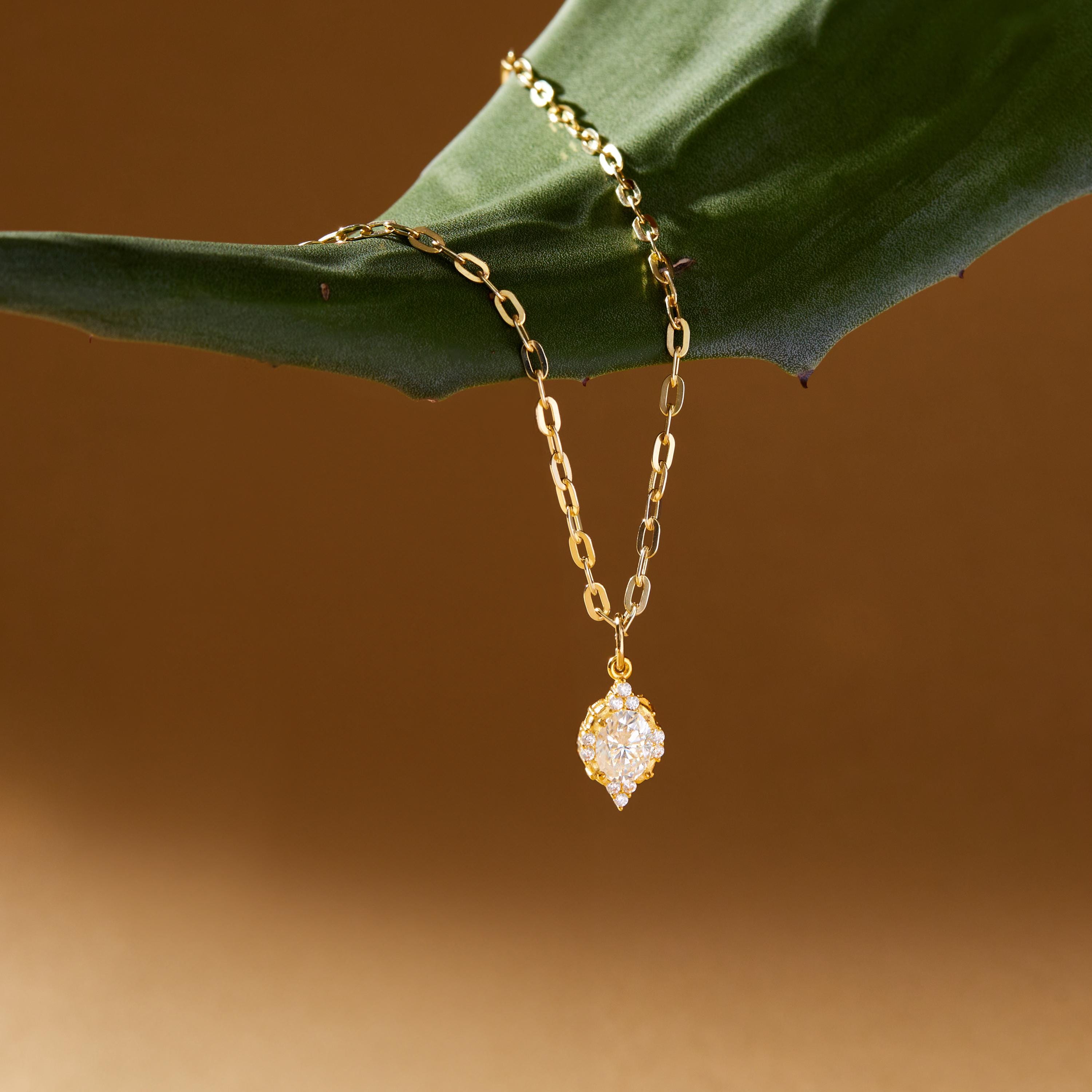 Gold chain necklace with a moissanite pendant on a green leaf against a brown background