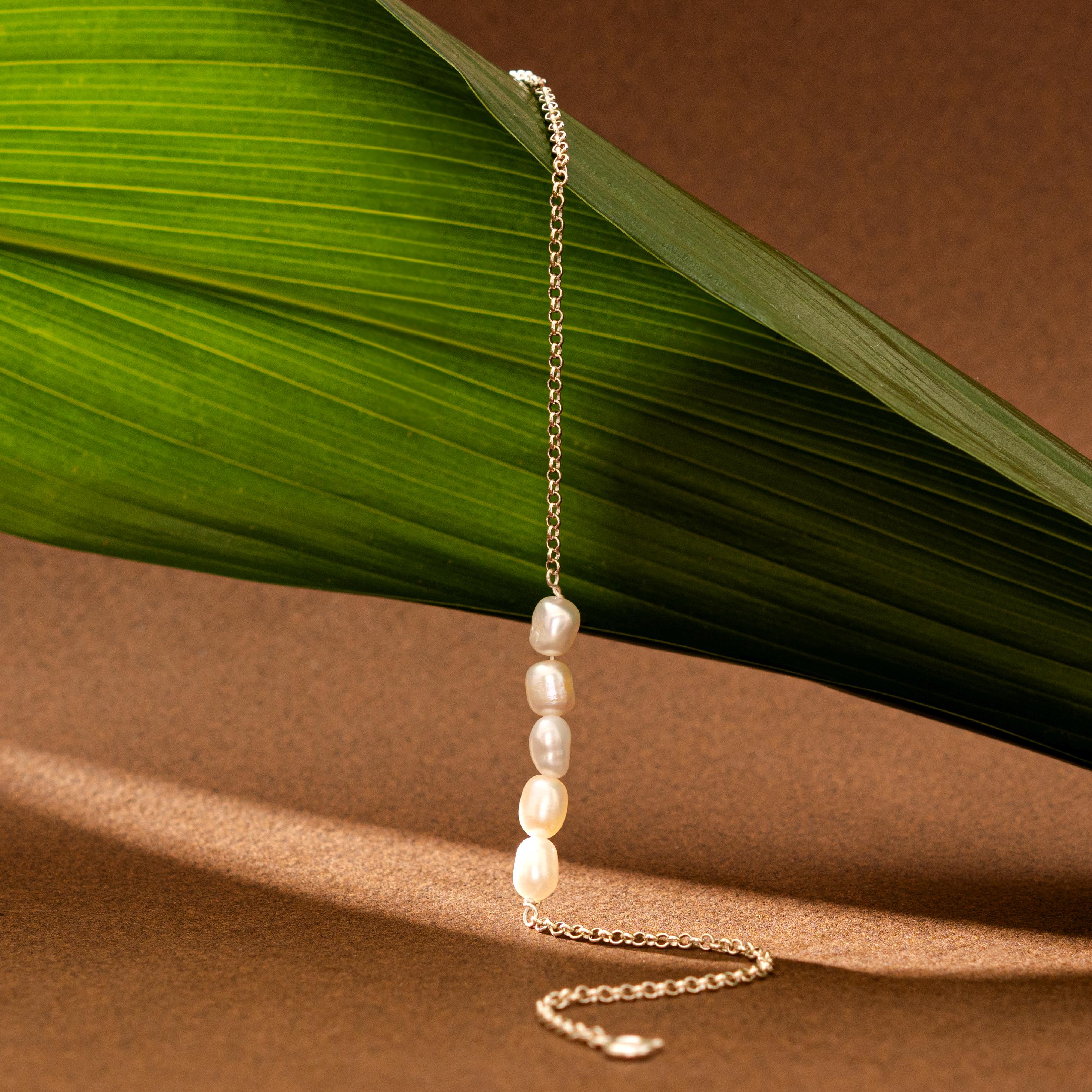 Pearl necklace on a chain with a green leaf on a brown background