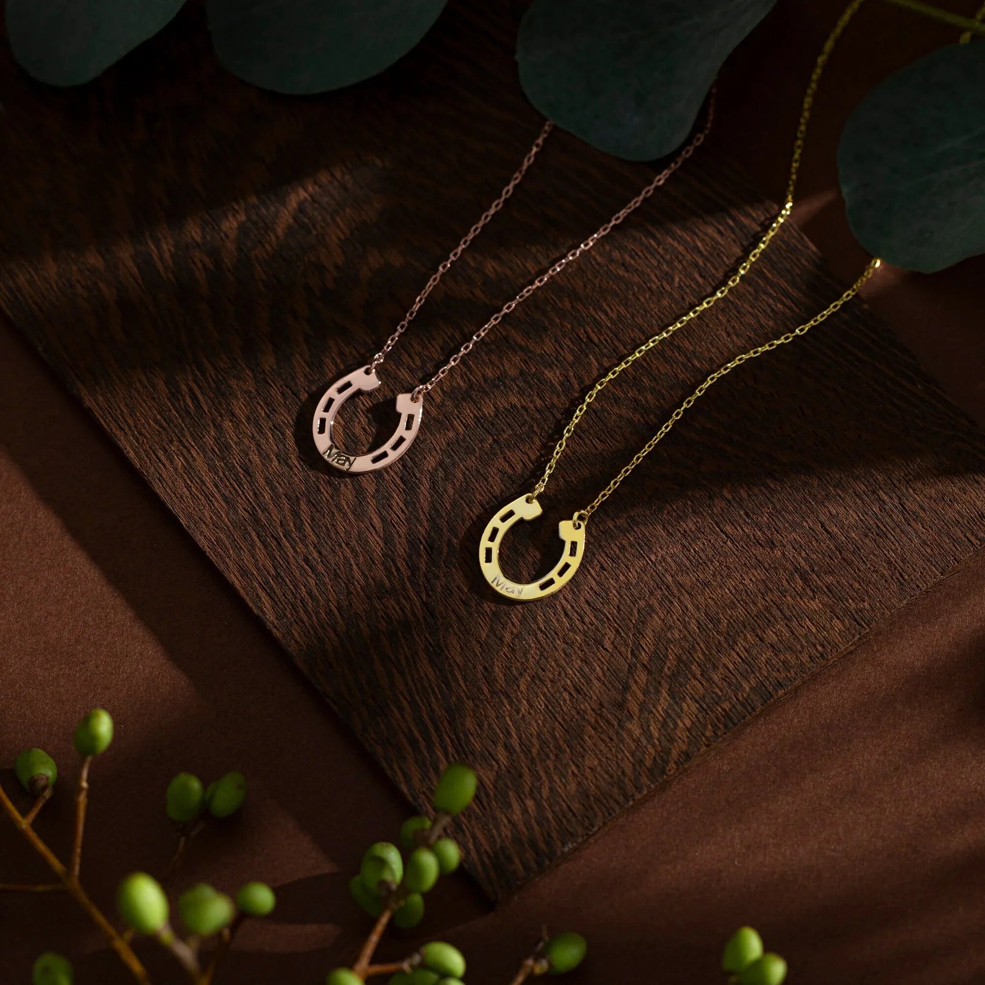 Two personalized horseshoe necklaces in rose gold and yellow gold displayed on a dark wooden surface