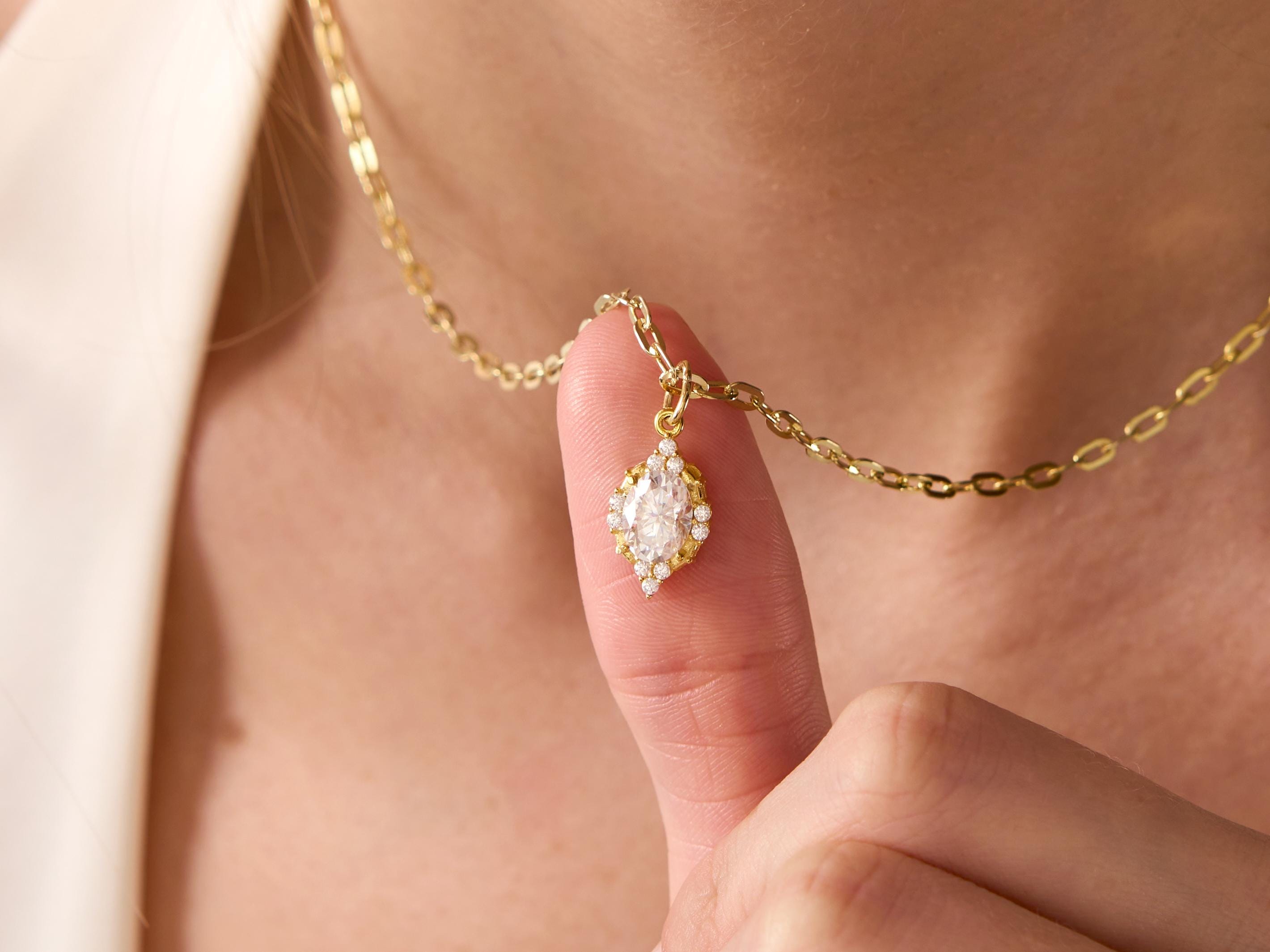 Gold necklace with a pendant held by a hand against a neutral background