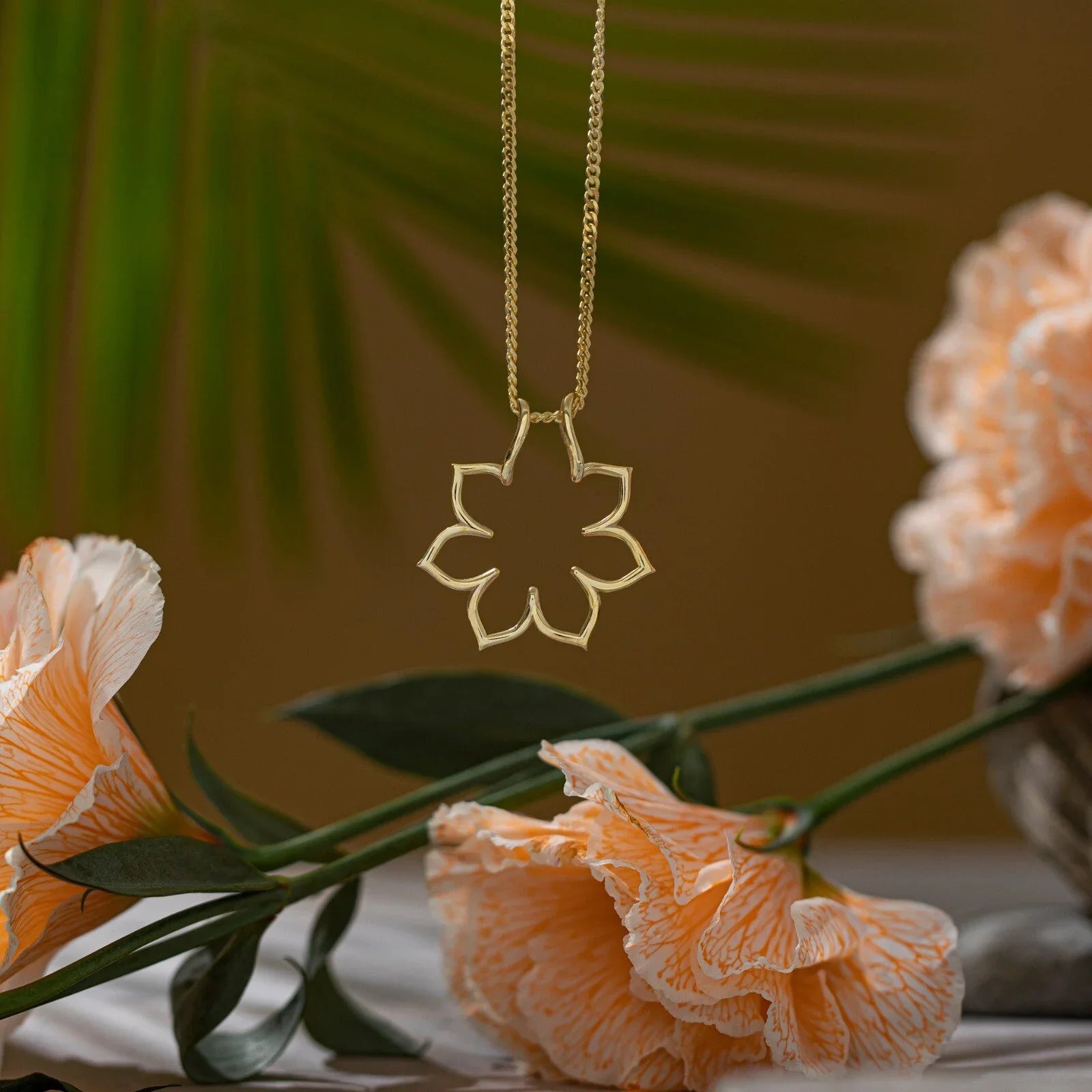 Gold floral pendant necklace with delicate peach flowers and tropical leaves background