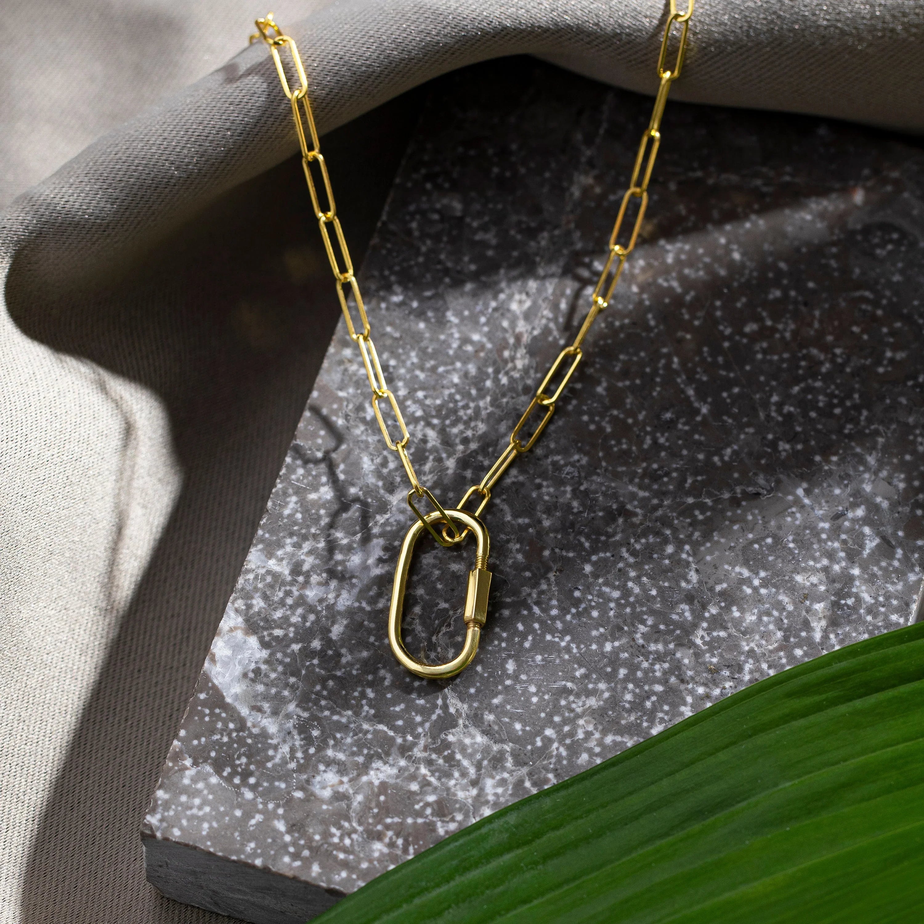 Gold paperclip chain necklace with oval clasp on a textured stone background