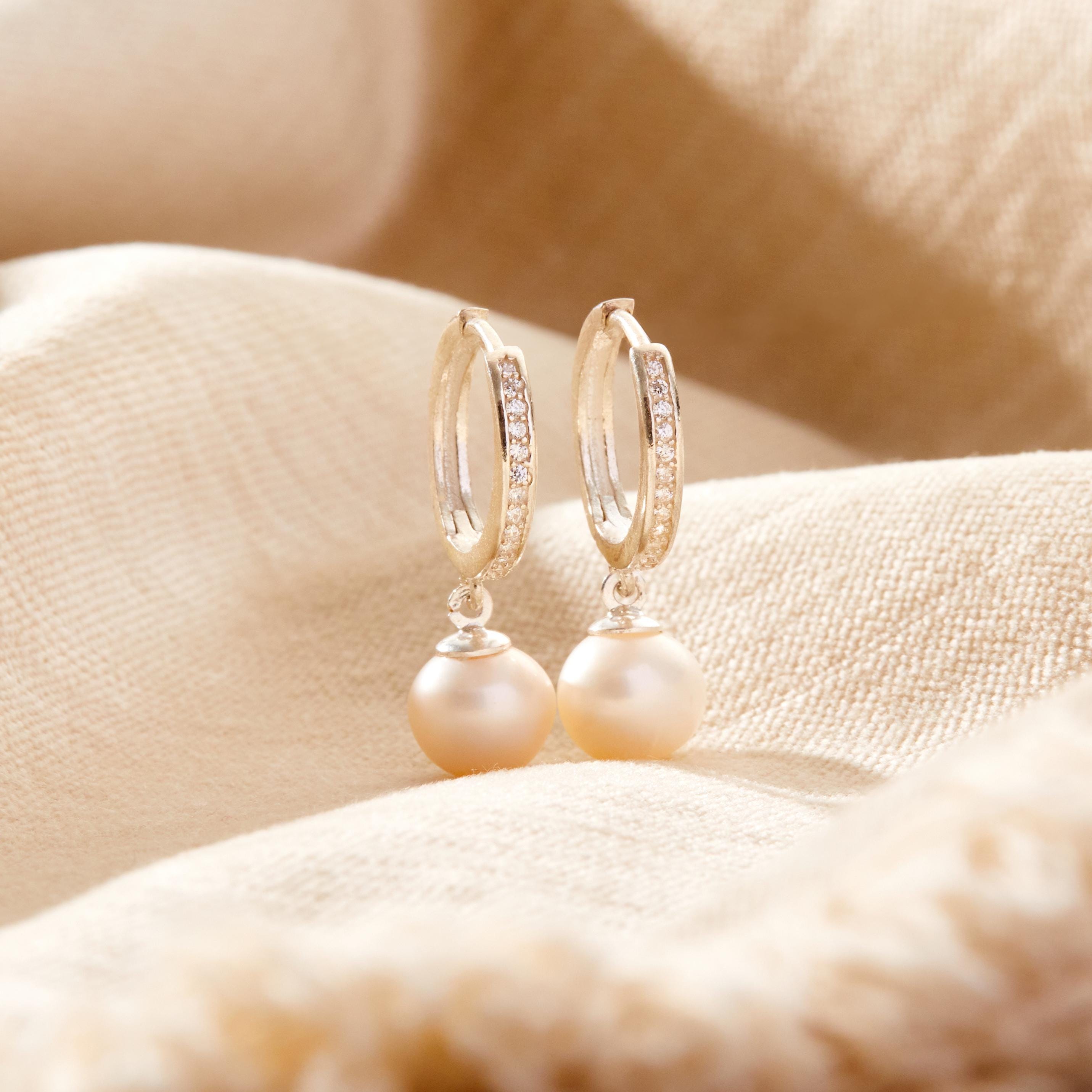 Pearl earrings with gold hoop designs on a soft beige fabric background